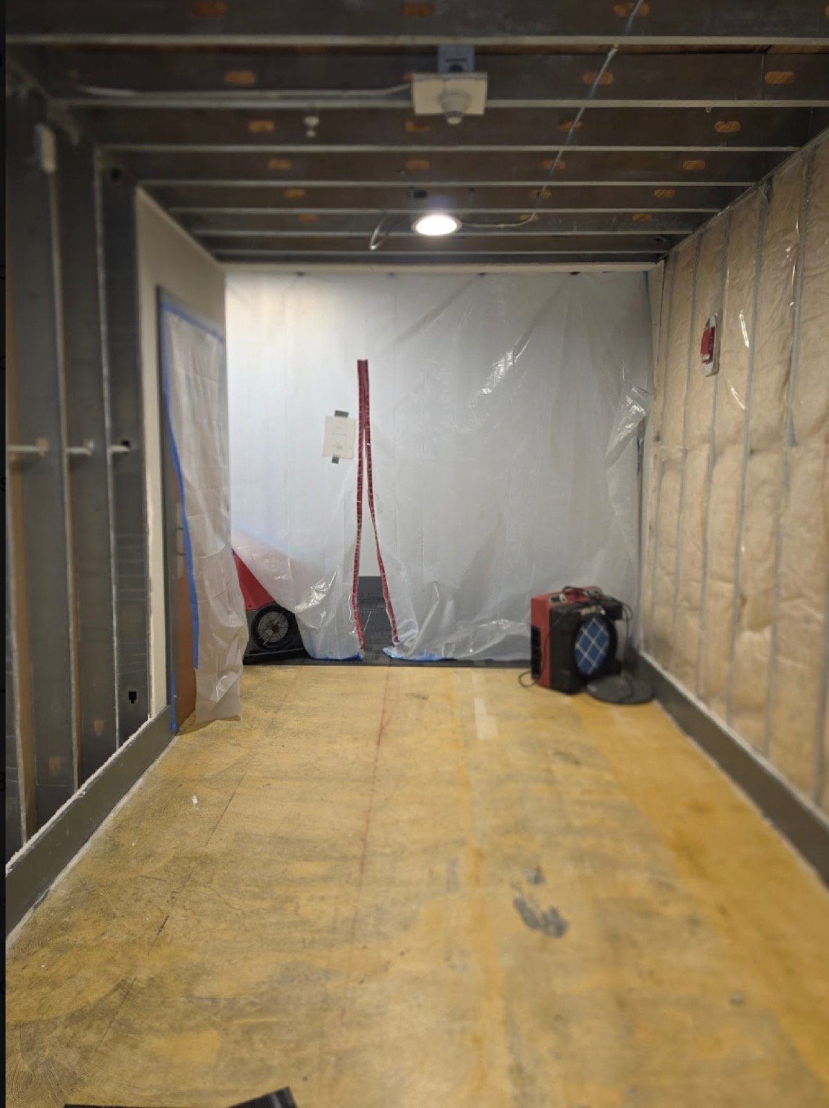 Commercial space stripped to metal studs and subfloor with containment barrier and air movers running